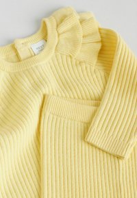 Pulover galben cu dungi și pantaloni asortați, având un guler ondulat și un material texturat. Ambele articole prezintă un aspect moale și confortabil.