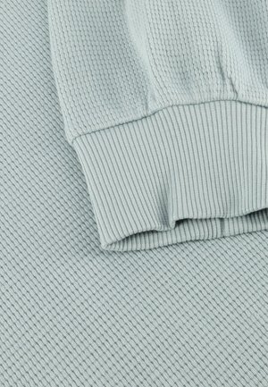 Lichtblauwe gebreide stof met geribbelde manchetdetail, met zichtbare textuur in het weefsel en opgevouwen mouwrand.