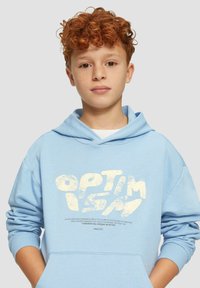 Lichtblauwe hoodie van zacht materiaal met een voorzak. Voorzien van een grote witte tekstafdruk in een informele lettertype en ribbelmanchetten.
