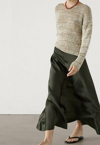 Pull en maille texturée beige clair à manches longues ; jupe en satin vert olive ; sandales fines noires ; accessoires discrets.