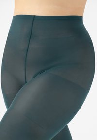 Collant di un profondo colore teal, realizzati in materiale trasparente con una texture liscia, design a vita alta, con una sottile cucitura tonale.