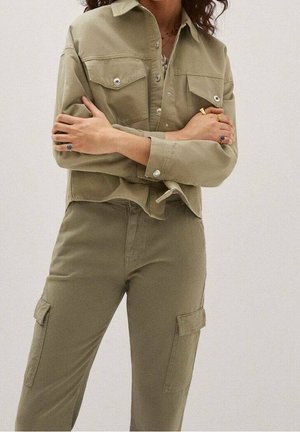 Oliivinvihreä puuvillapaita, jossa on nepparit ja rintataskut, yhdistettynä vastaaviin cargo-housuihin, joissa on sivutaskut ja kapea istuvuus.