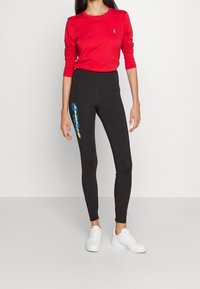 Röd långärmad topp och svarta leggings med blå och gula grafiska tryck på sidan, tillsammans med vita sneakers. Slät tyg, figurnära design.