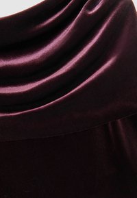 Tissu en satin d'un bordeaux profond, présentant une texture lisse et brillante avec des plis drapés et un bord supérieur arrondi et sans couture.