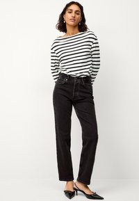 Gestreepte zwart-witte blouse met lange mouwen, gecombineerd met hooggerote zwarte jeans. De textuur is soepel; de jeans hebben een klassiek vijf-pocket ontwerp.