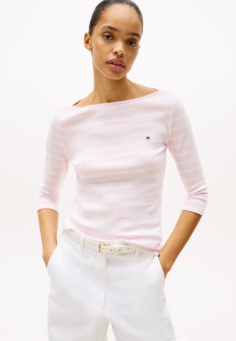 Rosa og hvit stripete langermet topp med off-shoulder utringning, kombinert med hvite høyt midje bukser og et hvitt belte.