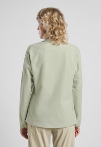 Giacca verde chiaro con maniche lunghe, dal tocco liscio e opaco, e un design del colletto semplice. Il retro presenta un taglio dritto e senza hardware visibili.