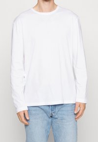 Camiseta blanca de manga larga hecha de algodón, con cuello redondo y un corte relajado, combinada con jeans de mezclilla azul claro.
