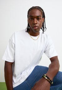 Hvid bomuld t-shirt med korte ærmer, prydet med et diskret logo. Kombineret med blå denim jeans og perlearmbånd på håndleddet.