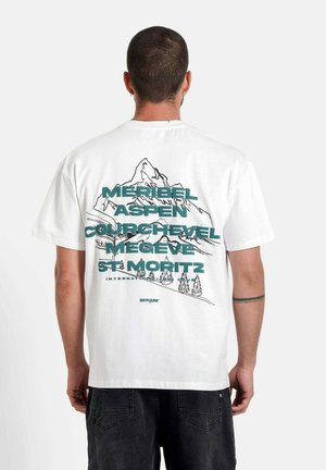 Witte katoenen T-shirt met een bergafbeelding en tekst in teal: "Méribel, Aspen, Courchevel, Megève, St. Moritz" op de achterkant.