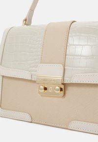 Sac bandoulière beige et crème avec rabat à texture crocodile, fermoir doré gravé "ANNA FIELD" et détail de sangle réglable.