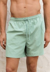 Pantaloni da bagno verde menta con cintura elastica, chiusura con cordoncino, vestibilità rilassata e tessuto leggero e testurizzato.