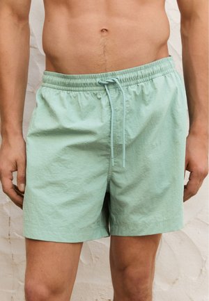 Shorts de bain vert menthe avec une taille élastique, fermeture à cordon, coupe décontractée et tissu léger et texturé.