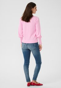 Ljusrosa tröja med långa, något puffiga ärmar, kombinerad med mörkblå slim-fit jeans och röda ballerina-skor. Enkel, slät textur.