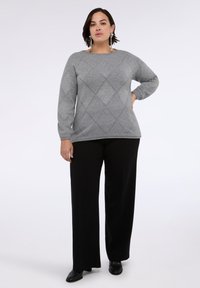 Szary sweter z dzianiny z wzorem diamentowych wycięć, długimi rękawami i okrągłym dekoltem, w połączeniu z czarnymi spodniami o szerokich nogawkach i czarnymi butami.