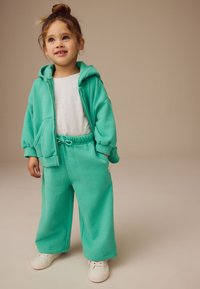 Turquoise hoodie and matching wide-legged sweatpants made of soft fabric, paired with white sneakers. Features a front pocket and drawstring waist.