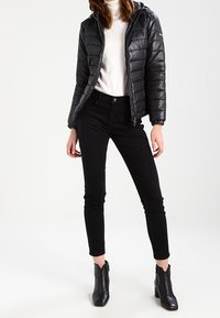 Zwarte pufferjas met capuchon, ritssluiting en doorgestikt patroon. Gecombineerd met zwarte skinny jeans en enkellaarsjes. Effen kleur, modern ontwerp.