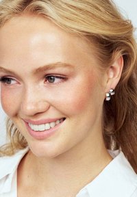 Silver studs med en rund, slät design och en blank yta, bärs av en person med ljusbrunt hår och en vit skjorta.