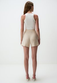 Weißes, geripptes Tanktop kombiniert mit beigen Shorts, die eine glatte Textur und eine lockere Passform aufweisen, mit mittelhohem Bund und Seitennähten.