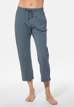 Onderlichaam van een blootsvoetse persoon die blauwe, ingekorte joggingbroeken draagt met een elastische tailleband en een trekkoord, tegen een witte achtergrond.