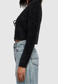 Pull noir, coupé, en matière moelleuse avec des manches longues et un nœud au niveau du col, associé à un jean taille haute bleu clair.