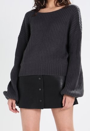 Grauer gerippter Strickpullover mit übergroßen Ärmeln, kombiniert mit einem schwarzen Leder-Minikleid mit fünf dekorativen Knöpfen.