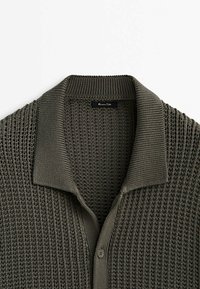 Cardigan en maille vert olive foncé avec un large col côtelé et deux boutons, affichant l'étiquette Massimo Dutti à l'intérieur de la zone du cou.