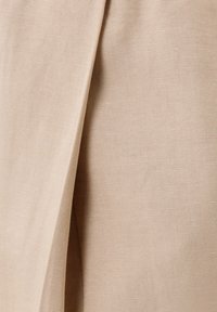 Tela beige con un pliegue diagonal, que muestra un tejido fino y texturizado y una superficie lisa bajo una iluminación suave.