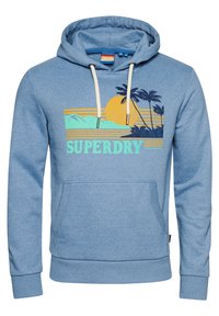 Sudadera azul claro con cordones blancos, bolsillo frontal y gráfico de atardecer tropical con palmeras y montañas sobre el texto "SUPERDRY".