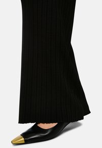 Black ribbed trousers with a wide leg design, paired with sleek black pointy-toed shoes featuring a metallic gold cap toe.