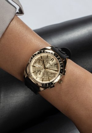 Montre dorée avec un cadran texturé doré et trois sous-cadrans, bracelet en caoutchouc noir, et "FURLA" gravé autour de la lunette.