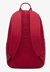 Κόκκινο υφασμάτινο σακίδιο πλάτης με επενδυμένους ιμάντες, με ανάγλυφο κείμενο "JORDAN" και μικρό πράσινο λογότυπο Jumpman στο πλάι.