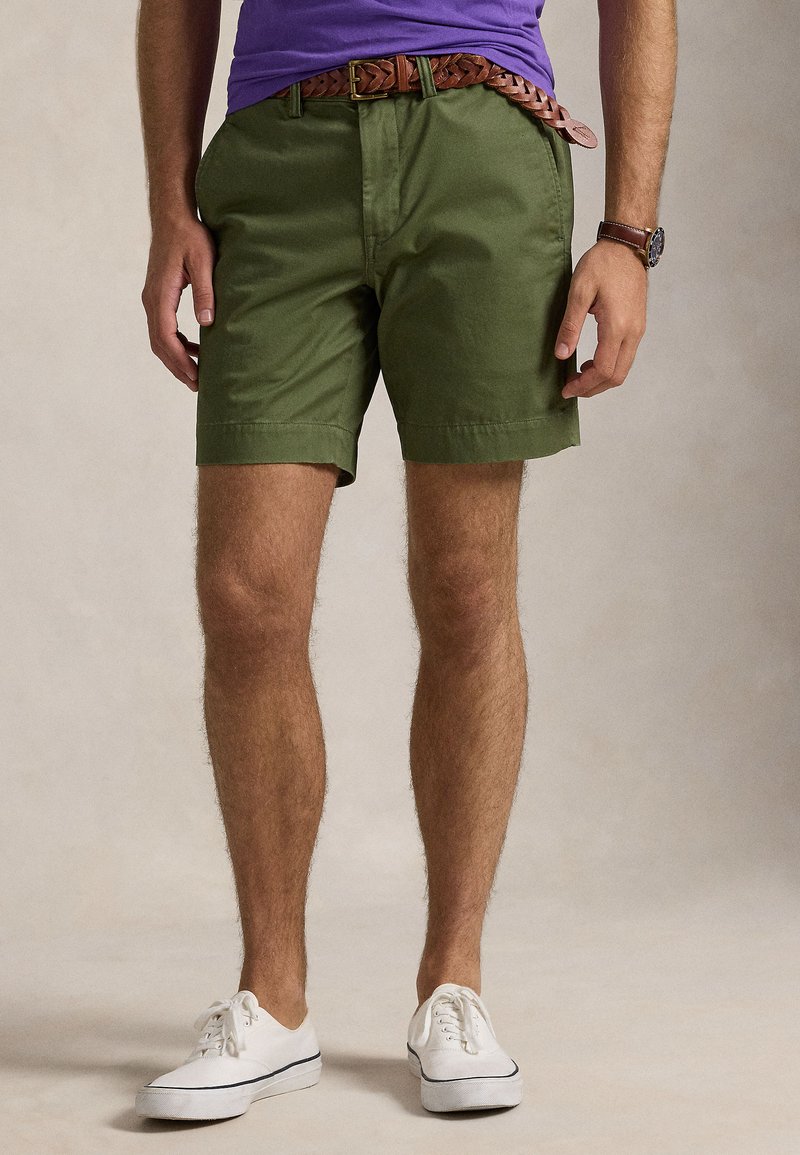 Zelené bavlnené šortky s voľným strihom, ohrnutými lemami a viazaným hnedým koženým opaskom, skombinované s bielymi plátenými topánkami.