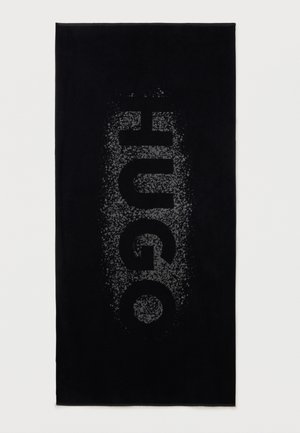 Melns taisnstūrveida dvielis ar zīmola nosaukumu "HUGO" lieliem, pelēkiem, punktainiem vertikāliem burtiem centrā.