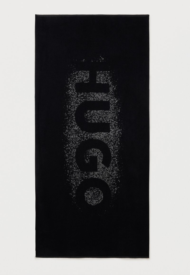 Μαύρη ορθογώνια πετσέτα με το όνομα της μάρκας "HUGO" σε μεγάλα, γκρίζα κάθετα γράμματα με βουβή υφή στο κέντρο.