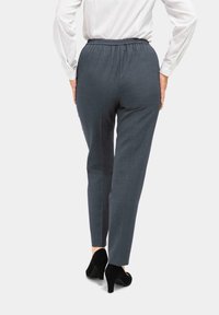 Graue gemusterte Hose mit elastischem Bund, schmal zulaufenden Beinen und glatter Textur, kombiniert mit schwarzen High-Heels.