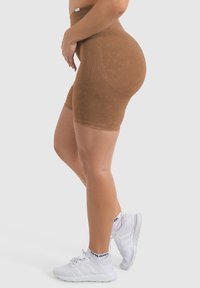 Shorts da ciclismo marroni a vita alta realizzati in tessuto texture con accenti a costine verticali, abbinati a scarpe da ginnastica bianche e calze con motivo.