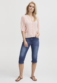 Camicia button-up rosa chiaro con righe verticali e maniche arricciate, abbinata a jeans cropped blu scuro e infradito marroni.