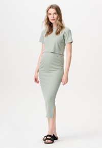 Hellgrün gestreifter Zweiteiler bestehend aus einem cropped Top und einem taillierten Rock mit seitlichen Schlitzen, kombiniert mit schwarzen Sandalen.