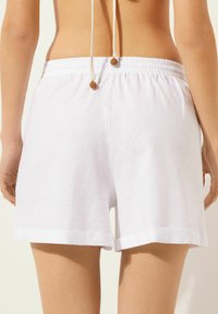 Hvide linned shorts med elastisk talje, opfoldet kant og en snortræk accent med teksturerede perler bagpå.