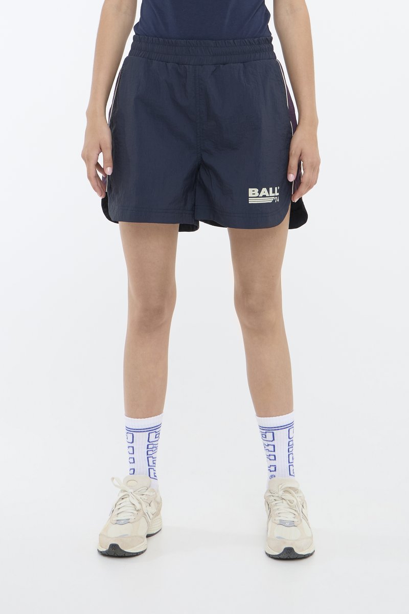 Marine blå treningsshorts med elastisk midje, med en hvit "BALL"-logo. Kombinert med mønstrede blå og hvite sokker og beige sko.
