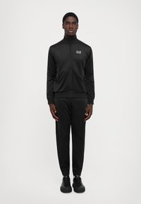 Black athletic tracksuit made of sleek, lightweight material. Features a zip-up jacket and tapered pants, both with snug wrist and ankle cuffs.