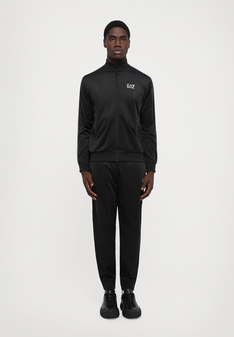 Black athletic tracksuit made of sleek, lightweight material. Features a zip-up jacket and tapered pants, both with snug wrist and ankle cuffs.