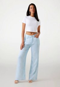 Balta īsa T-krekla ar gaisīgi zilām platām biksēm. Abu priekšmetu tekstūra ir gluda un dizains ikdienišķs.