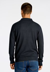 Svart stickad tröja med långa ärmar och krage. Mjuk textur, figurnära design samt ribbade muddar och nederdel. Bärs med blå jeans.