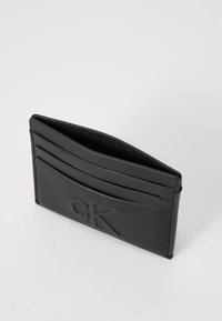 Portafoglio in pelle nera con logo "CK" in rilievo, dotato di più scomparti per carte e una texture liscia. Design compatto e minimalista.