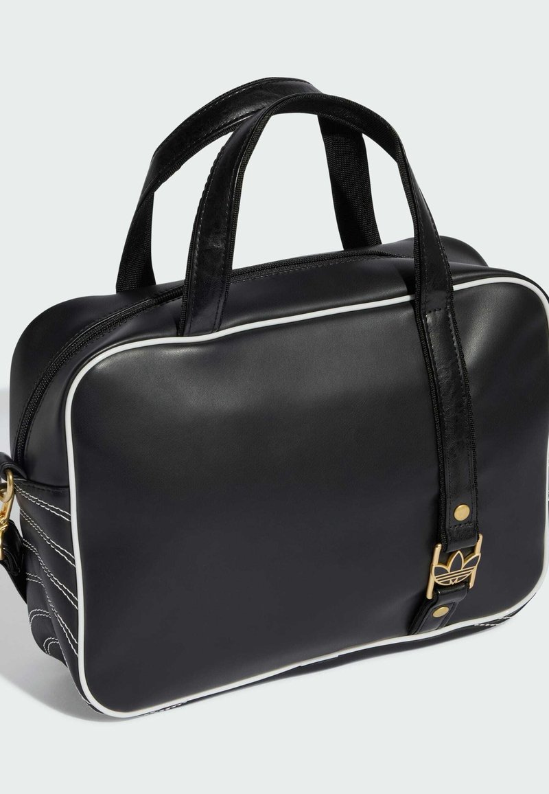 Sac à main rectangulaire noir avec bordure blanche, double poignée supérieure, boucle dorée avec logo trèfle et fermeture éclair sur le dessus.