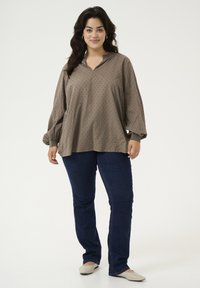 Bruine blouse met lange mouwen, een v-hals en een gestructureerd patroon, gecombineerd met donkerblauwe jeans en beige ballerina's, met een ontspannen pasvorm.