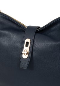 Borsa a pochette in pelle blu navy con superficie texture, hardware dorato e chiusura con zip. Presenta un flap decorativo con un gancio ad anello.