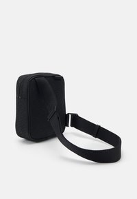 Zwarte schoudertas van gestructureerde stof, met een subtiel logo-patroon, ritssluiting en verstelbare schouderband.